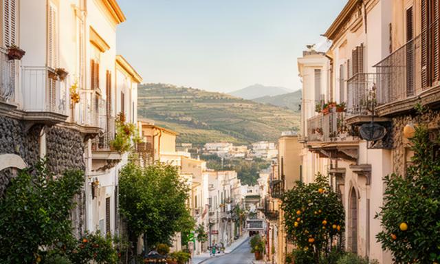Strada del centro di Valverde in Sicilia con edifici chiari, vegetazione mediterranea e luce del pomeriggio