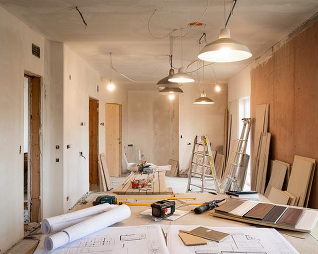 Cantiere di ristrutturazione interno con tavole progettuali, lampade e pareti in fase di finitura